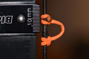 Wanneer je de meethaak op de pijlenopleggen legt, dient de onderkant van de nok gelijk te komen met het nulpunt van de meethaak. De reden hiervoor is is omdat je je pijl eerst perfect center gelegd hebt t.o.v. de gaten in de boog, daardoor komt de onderkant van de pijl iets lager te liggen dan het meetkundige centrum. Je meethaak zal dus zelf ook iets onder het meetkundige centrum van je boog liggen... vandaar dat de "0" (nul) gelijk moet liggen met de onderkant van je nok. Het centrum van je nok zal dan in het centrum van je boog liggen, dus iets boven de "0".